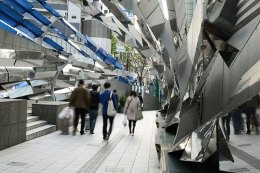 Tokyo 'da kentsel çevreye entegre yansıtıcı metal ve açısal yapıların yer aldığı modern bir sanat kurulumu. Yakınlarda yürüyen yayalar sanatın ve günlük yaşamın uyumu üzerinde dururlar..