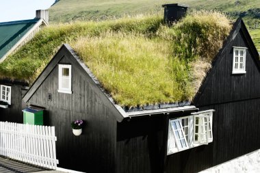 Faroe Adaları 'nda geleneksel bir çim çatılı ev, siyah ahşap dış, beyaz çerçeveli pencereler, ve yeşil tepelere karşı izolasyon ve sürdürülebilirlik için tasarlanmış canlı yeşil çatı.