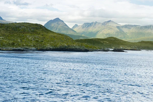 Patagonya 'daki Beagle Kanalı' nın sakin dalgalı suları, kayalık bitki örtülü adaları ve alçak bulutların altında engebeli zirveleri olan görkemli bir dağ sırası..