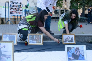 Bükreş, Romanya - 09 / 21 / 2025: İki kadın, 21 Aralık 'ta Romanya' nın Bükreş kentinde düzenlenen Filistin dayanışma gösterisinde Filistin bayrağı anma töreninde çerçeveli fotoğrafların yanına mum koydu.