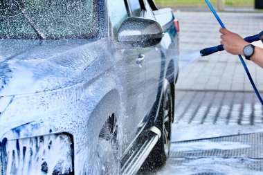 Adam yüksek basınçlı bir arabayı özel yıkamayla temizliyor..