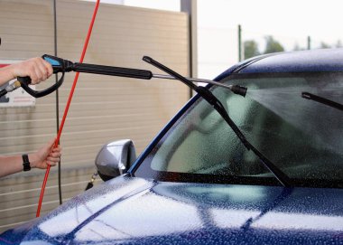 Adam araba yıkamada arabayı yıkıyor.