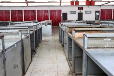 Arka planda metal tezgahlar ve kapalı kırmızı yuvarlanan kapılar olan boş bir geleneksel marketin kapalı bir fotoğrafı. Piyasa, temiz döşeme döşemeleri ve çelik çerçeveli tezgahlarıyla ıssız görünüyor.