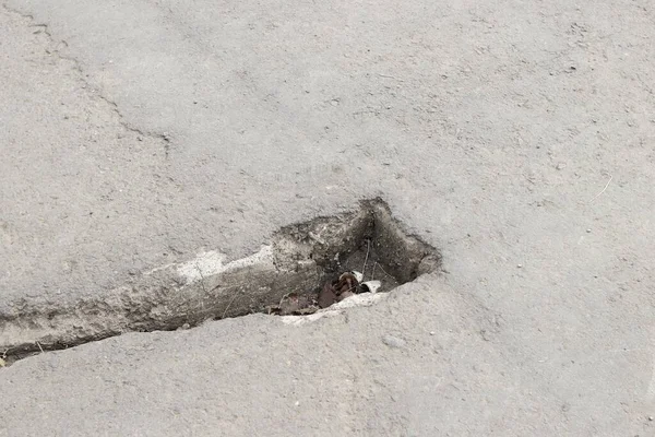 Çukur kazılmış asfalt yol. Hasarlı yolun tamir edilmesi gereken yakın plan fotoğrafı. Doku ve arkaplan gri renkte..