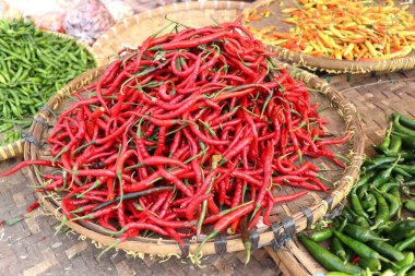 Kıvırcık kırmızı biberler, yeşil kuş gözü biberler ve geleneksel bir markette ahşap tepside kırmızı kuş gözü biberler. Arka plan baharatlı ve taze kırmızı biberlerle dolu. Asya 'da önemli bir bileşen.