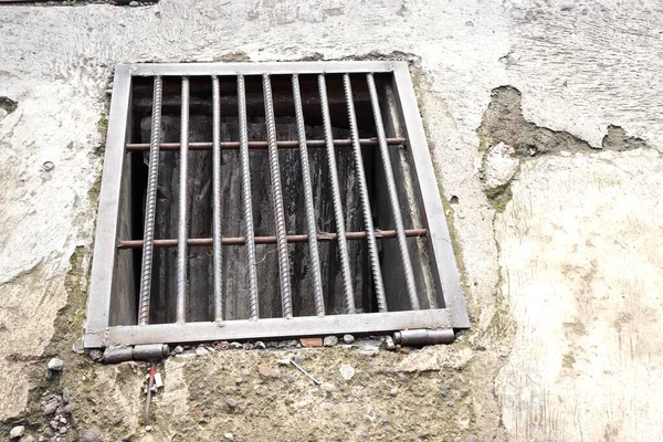 Çürümüş beton kaldırıma metal drenaj ızgarası döşenmiş. Dikdörtgen drenaj kapağı, kenarlarında görünen pas, toprak ve aşınma ile kalın çelik parmaklıklardan yapılmıştır..