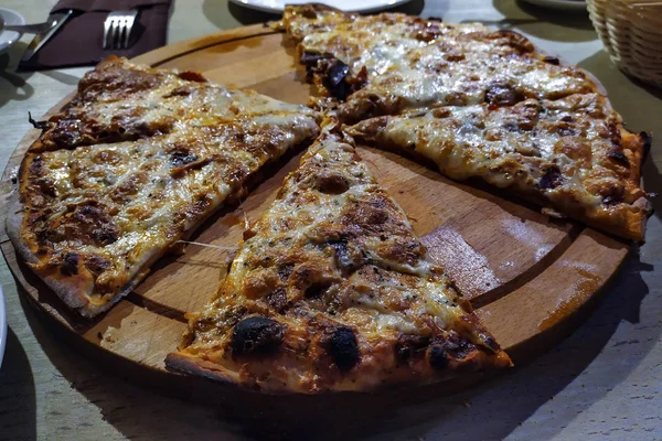 Pizza ronde coupée en morceaux sur un plateau en bois rond . — Photo