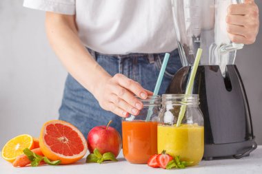 Kadın çok renkli yaz meyve suları ya da iki yüzlü cam kavanoz ve malzemelerin üzerine beyaz masa yemek.