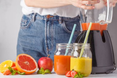 Kadın çok renkli yaz meyve suları ya da iki yüzlü cam kavanoz ve malzemelerin üzerine beyaz masa yemek.