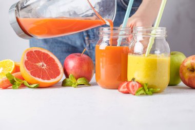 Kadın çok renkli yaz meyve suları ya da iki yüzlü cam kavanoz ve malzemelerin üzerine beyaz masa yemek.