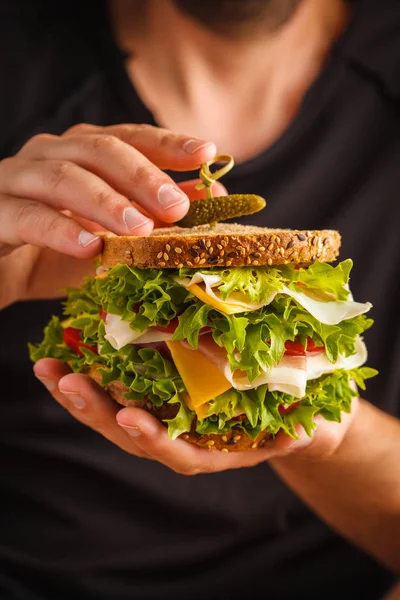 Ekmek, et (porshutto), peynir ve taze sebze erkek ellerini, koyu arka plan ile büyük sandviç.