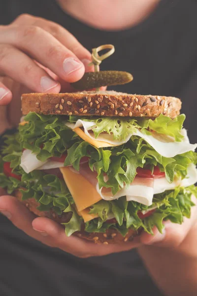 Ekmek, et (porshutto), peynir ve taze sebze erkek ellerini, koyu arka plan ile büyük sandviç.