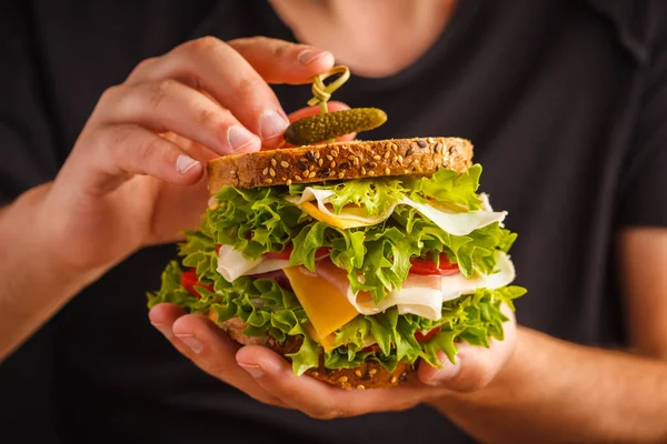 Ekmek, et (porshutto), peynir ve taze sebze erkek ellerini, koyu arka plan ile büyük sandviç.