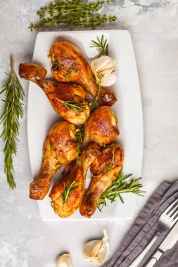 Sarımsak, biberiye ve kekik beyaz arka plan üzerinde beyaz tabak pişmiş ızgara baharatlı tavuk budu.