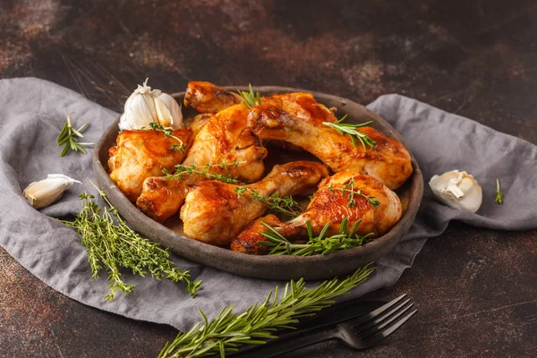 Grilled spicy chicken legs baked with garlic, rosemary and thyme in dark dish on dark background.