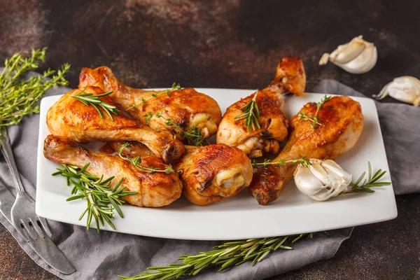 Sarımsak, biberiye ve kekik koyu arka plan üzerinde beyaz plaka ile pişmiş ızgara baharatlı tavuk budu.
