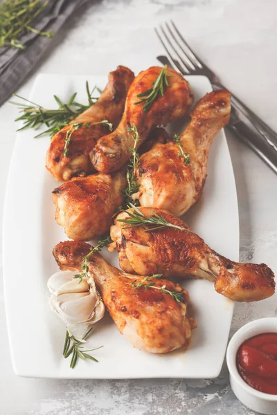 Grilled spicy chicken legs baked with garlic, rosemary and thyme in dark dish on white background.