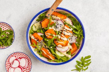 Gökkuşağı vegan salata roka, tatlı patates, turp, tahin sosu ve salatalık, beyaz arka plan ile. Sağlıklı vegan gıda kavramı.