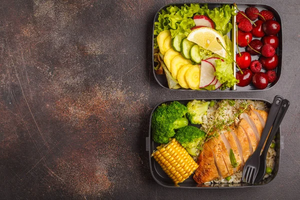 Healthy meal prep containers with grilled chicken with fruits, berries, rice and vegetables. Takeaway food jn dark background, top view