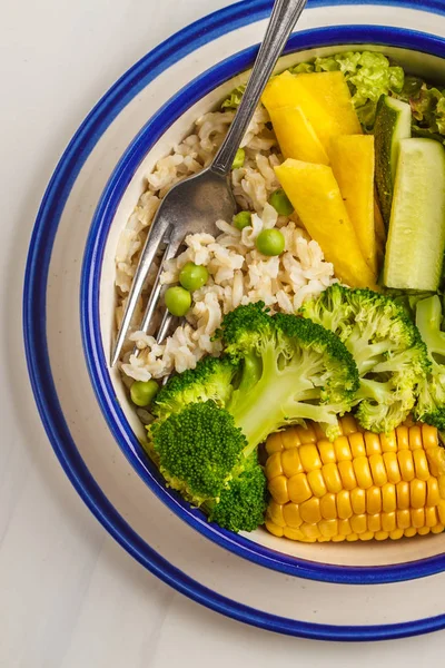 Healthy lunch with rice and vegetables. Vegan buddha bowl with brown rice, broccoli and vegetables in a white plate on a white background.