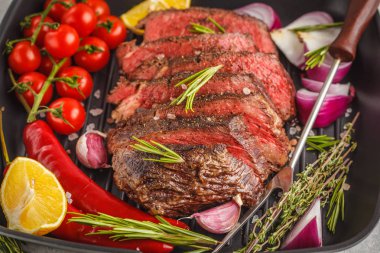 Baharat ve sebzeler, koyu arka plan ile bir tavada kızarmış biftek dilimlenmiş.