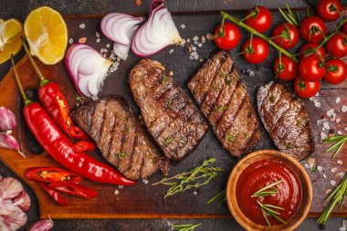 Izgara Dana biftek ile baharat ve sebzeler ahşap kesme tahtası, koyu arka plan, üstten görünüm