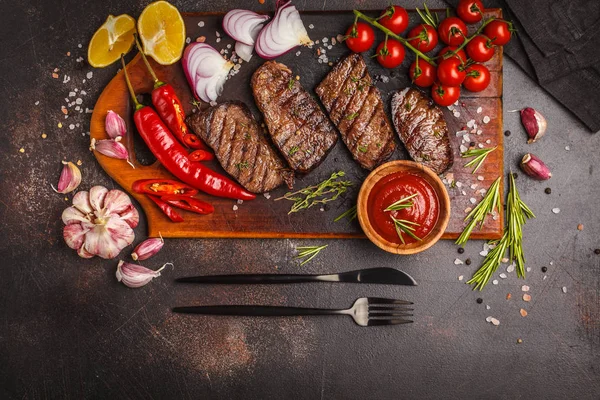 Izgara Dana biftek ile baharat ve sebzeler ahşap kesme tahtası, koyu arka plan, üstten görünüm