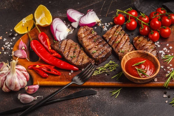 Izgara Dana biftek ile baharat ve sebzeler ahşap kesme tahtası, koyu arka plan, üstten görünüm