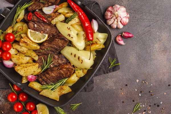 Fırında patates ve sebzeler bir pan ızgara, koyu arka plan, üstten görünüm ile sığır eti biftek ızgara.