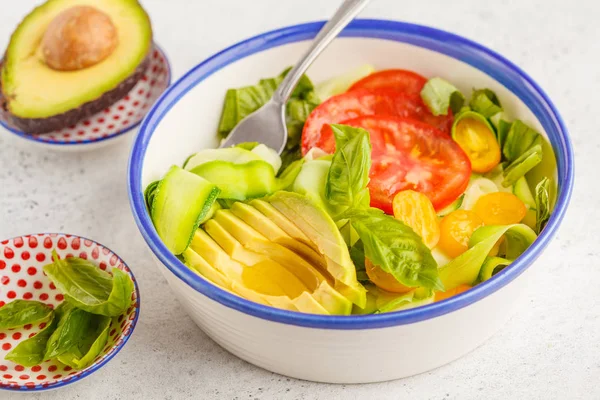 Green zucchini noodles salad with tomatoes, avocado and basil. Healthy vegan zucchini pasta. Clean eating concept.