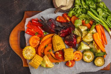 Pişmiş sebze: balkabağı, pancar, havuç, biber, kabak ve Mısır, üstten görünüm, koyu arka plan.