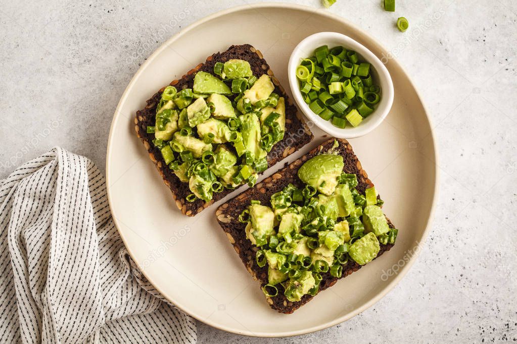 Avocado toast with whole wheat bread, avocado and green onion on a white plate. Clean eating concept.