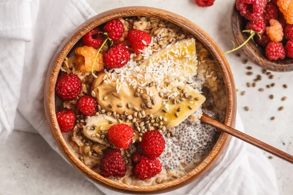 Oatmeal porridge with chia seeds, berries, peanut butter and hemp seeds in wooden bowl. Vegan healthy food concept.