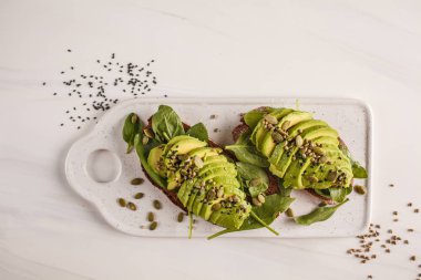 Kenevir tohumu, susam ve beyaz mermer tahtası, üstten görünüm kabak çekirdeği ile avokado tost. Bitki esaslı diyet kavramı.