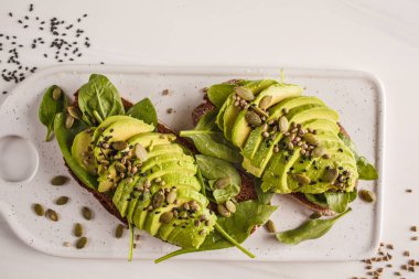 Kenevir tohumu, susam ve beyaz mermer tahtası, üstten görünüm kabak çekirdeği ile avokado tost. Bitki esaslı diyet kavramı.