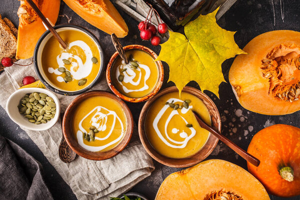 Autumn pumpkin soup puree with cream in cups, the autumn scenery. Healthy vegan food concept. Autumn food concept.