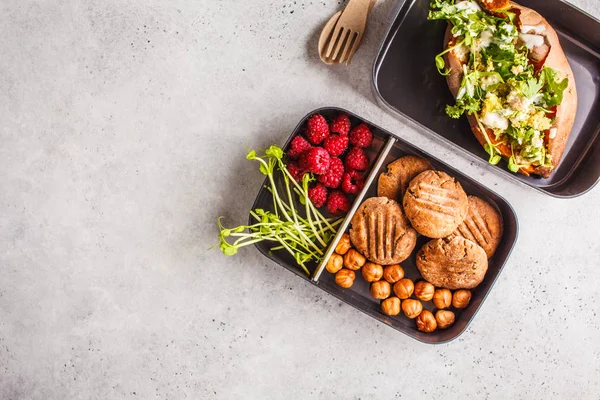 Healthy meal prep containers with quinoa Stuffed Sweet Potatoes, cookies, nuts and berries, overhead shot with copy space.