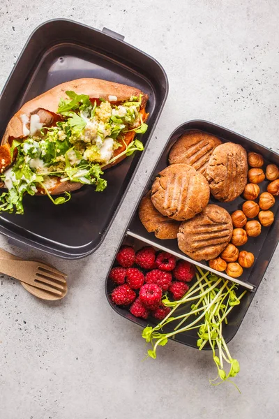 Healthy meal prep containers with quinoa Stuffed Sweet Potatoes, cookies, nuts and berries, overhead shot