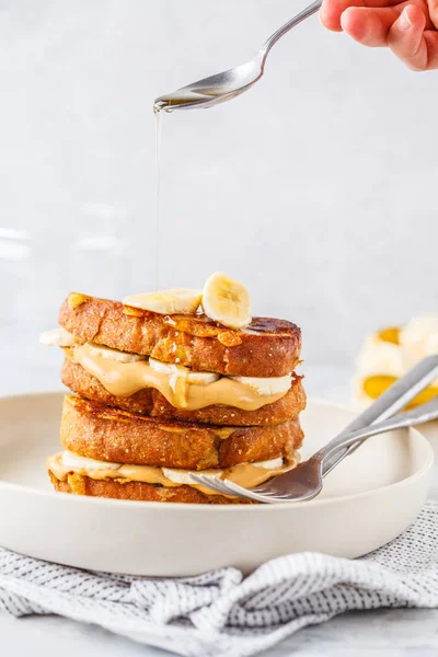 Vegan french toasts with peanut butter, syrup and banana on a white plate.