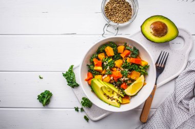 Vegan pirinç, kale, pişmiş kabak, havuç ve beyaz ahşap zemin üzerinde beyaz kase avokado salatası. Üstten görünüm, kopya alanı.