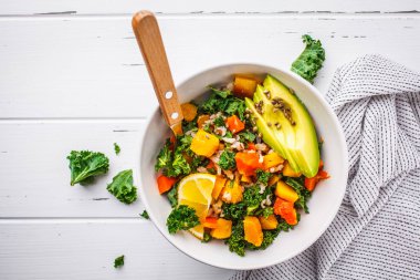 Vegan pirinç, kale, pişmiş kabak, havuç ve beyaz ahşap zemin üzerinde beyaz kase avokado salatası. Üstten görünüm, kopya alanı.