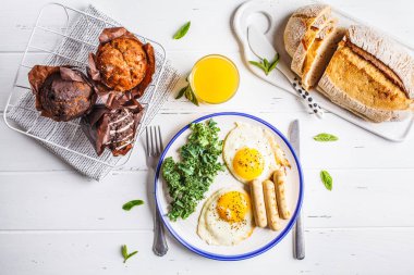 Sahanda yumurta, salata, kekler ve beyaz ahşap masa, üstten görünüm, kopya alanı portakal suyu ile sunulan kahvaltı.
