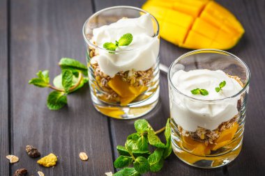 Bir bardak koyu ahşap arka plan üzerinde Yunan yoğurt mango granola parfe.