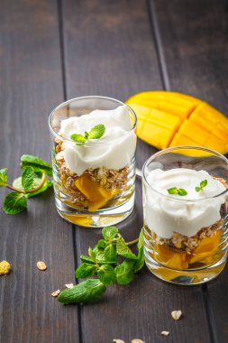 Bir bardak koyu ahşap arka plan üzerinde Yunan yoğurt mango granola parfe.