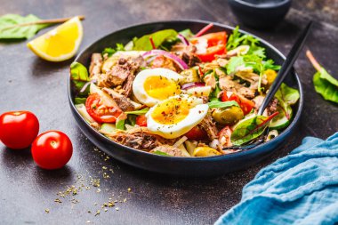 Ton balıklı makarna, zeytin, sebze ve karanlık bir arka plan siyah bir tabağa haşlanmış yumurta salatası.