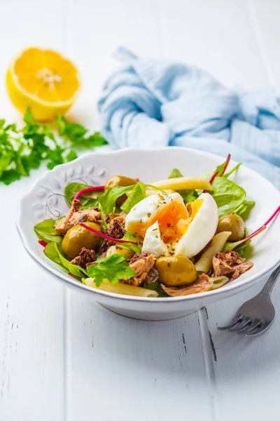 Ton balığı salatası makarna, zeytin ve beyaz ahşap zemin üzerinde beyaz bir tabak içinde haşlanmış yumurta.