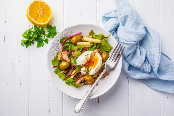 Ton balığı salatası makarna, zeytin ve beyaz ahşap zemin üzerinde beyaz bir tabak içinde haşlanmış yumurta.