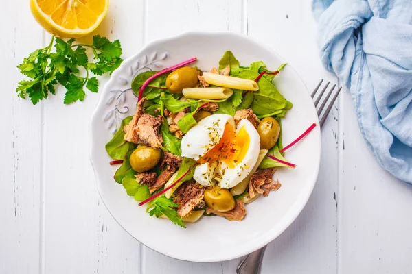 Ton balığı salatası makarna, zeytin ve beyaz ahşap zemin üzerinde beyaz bir tabak içinde haşlanmış yumurta.