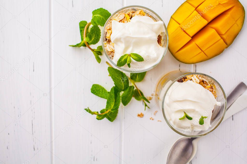 Greek yogurt mango granola parfait in a glass on a white wooden background, top view, copy space.