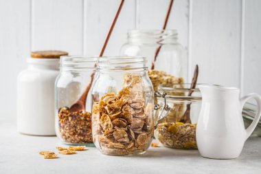 Ham kahvaltılık tahıllar: granola, müsli, cam kavanoz, beyaz arka planda yulaf ezmesi.